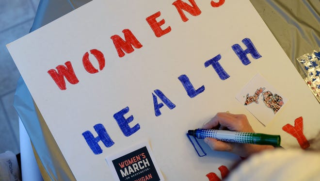 Tali Wendrow of West Bloomfield colors in letters on her sign to read "Women's Health is Family Health" on Sunday, Jan. 8, 2017 at a sign-making party at a home in Novi. The women made protest signs for the upcoming Women's March on Washington.