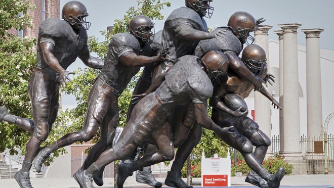 A hand sanitizing station is placed behind a statue of football players outside Memorial Stadium in Lincoln, Neb., Tuesday.