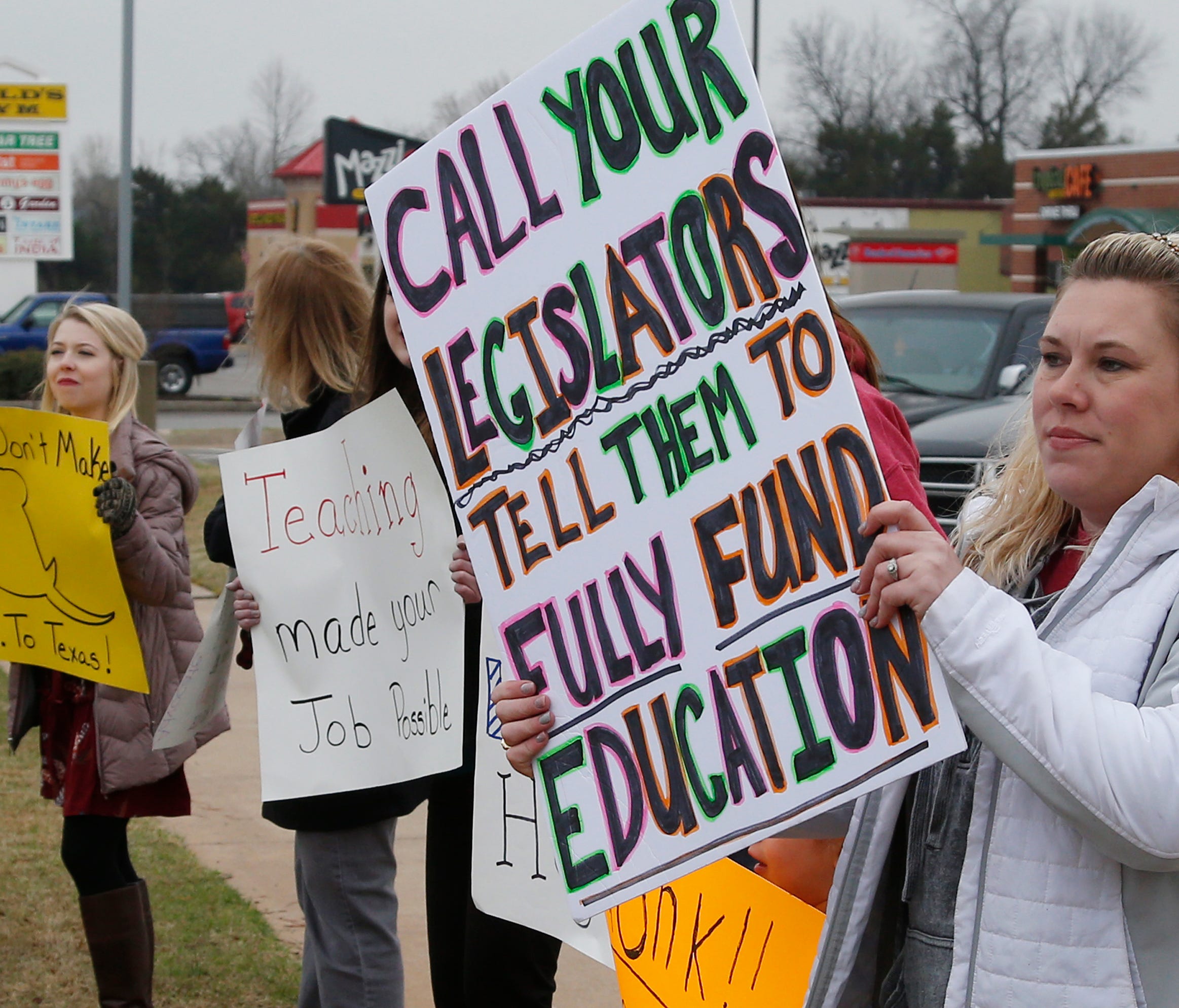 In this Tuesday, March 27, 2018, photo, teacher Adrien Gates pickets with other educators on a street corner in Norman, Okla.