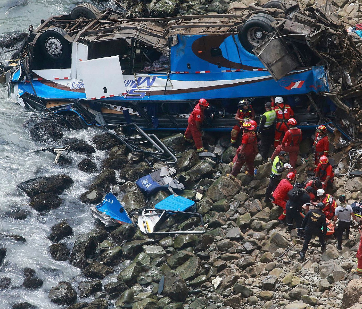 In this photo provided by the government news agency Andina, firemen recover bodies from a bus that fell off a cliff after it was hit by a tractor-trailer rig, in Pasamayo, Peru, Jan 2, 2018. A Peruvian police official says at least 25 people died, a