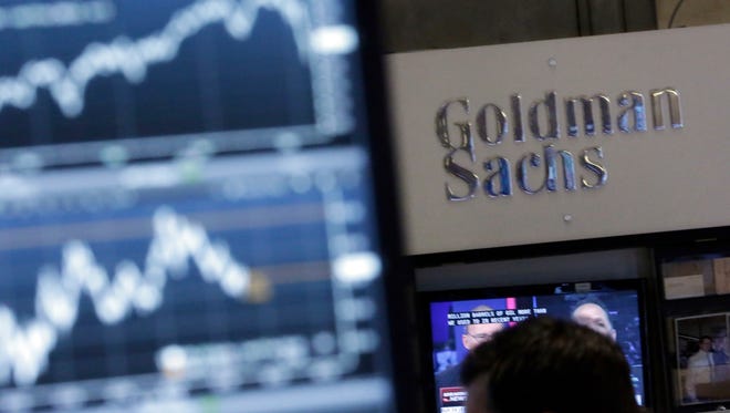 In this Oct. 16, 2014, file photo, a screen at a trading post on the floor of the New York Stock Exchange is juxtaposed with the Goldman Sachs booth.