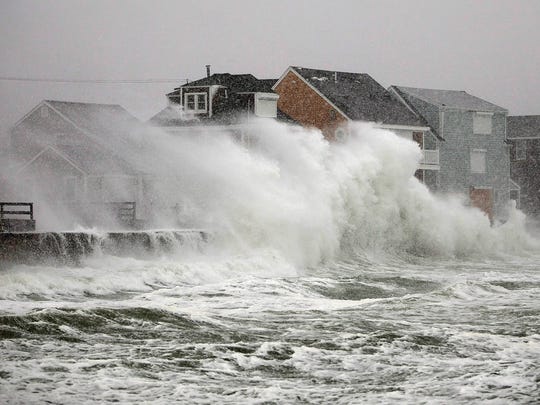 Waves crash over homes along the seawall in Scituate,