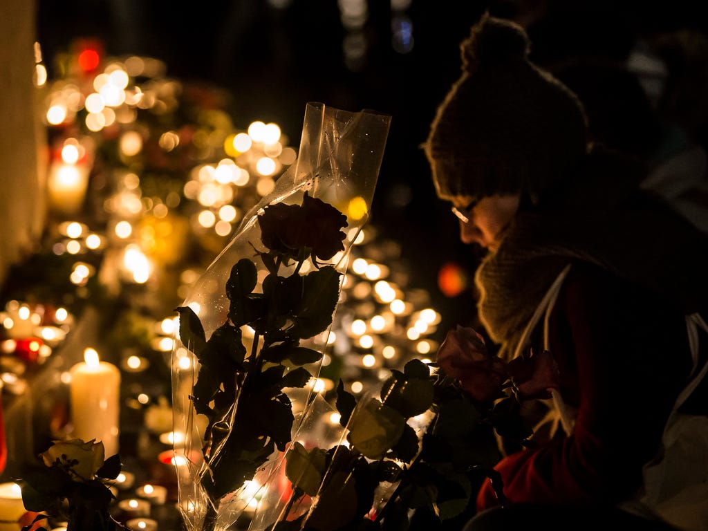 A  woman prays next to a silhouetted rose and candles at the monument on Place de la Republique in Paris as part of a spontaneous outpouring to mark the one-year anniversary of the attacks in Paris, Nov. 13, 2016.