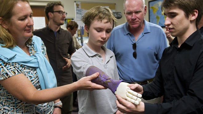 Wyatt Falardeau, 12, center, tries on a 3D-printed prosthetic arm with the help of his parents, Cynthia, left, Jim, right, and Tyler Petresky, Director of Resource Management at Limbitless Solutions, far right, at the University of Central Florida on Monday, February 16, 2015.  Wyatt's right forearm and hand were amputated shortly after birth.  He was recently selected by Limbitless to receive a 3D-printed arm similar to this one. Limbitless hopes to have it done by the summer.
(MOLLY BARTELS/TREASURE COAST NEWSPAPERS)