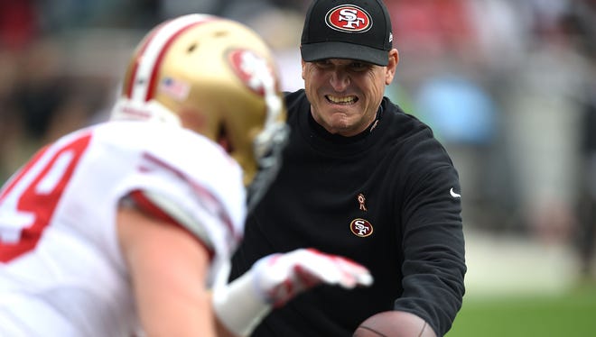 Coach Jim Harbaugh of the San Francisco 49ers hands off during pregame warm-ups Dec. 7, 2014, in Oakland, California.
