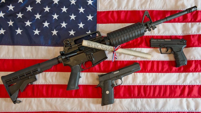 A photo illustration shows a Colt AR-15 semi-automatic rifle, a Colt .45 semi-automatic handgun, a Walther PK380 semi-automatic handgun and a copy of the Constitution on top of the American flag.