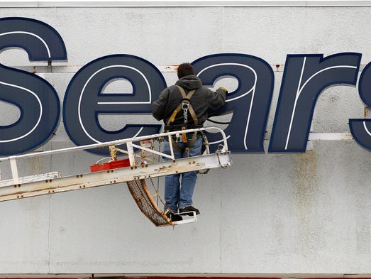A worker repairs the sign outside the Sears Grand store