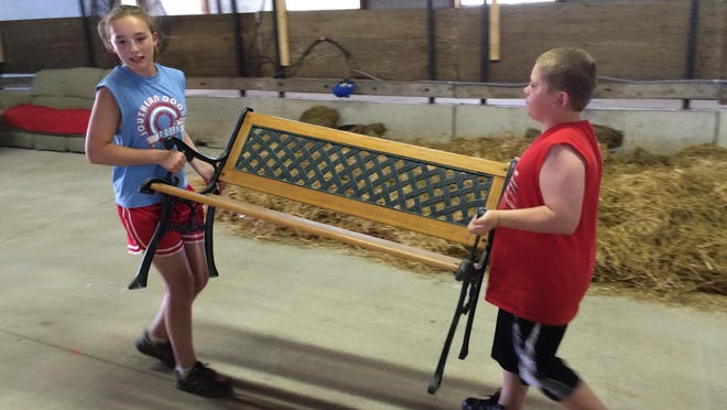 Cousins Chloe LaCrosse and Riley Phillips move a bench Monday night, which will sit near their family’s Holsteins in the Door County Fair dairy barns.
