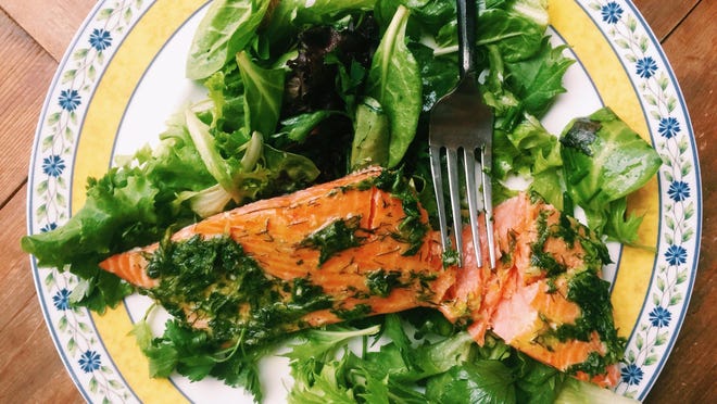 A fillet of salmon smothered in an herb marinade is served over a tender green salad. .