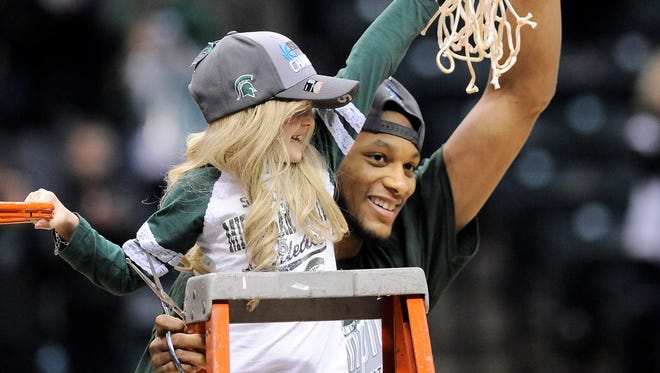 Michigan State forward Adriean Payne celebrates the Spartans' win against Michigan in the Big Ten Tournament along with Lacey Holsworth, age 8, as they hold one of the nets.