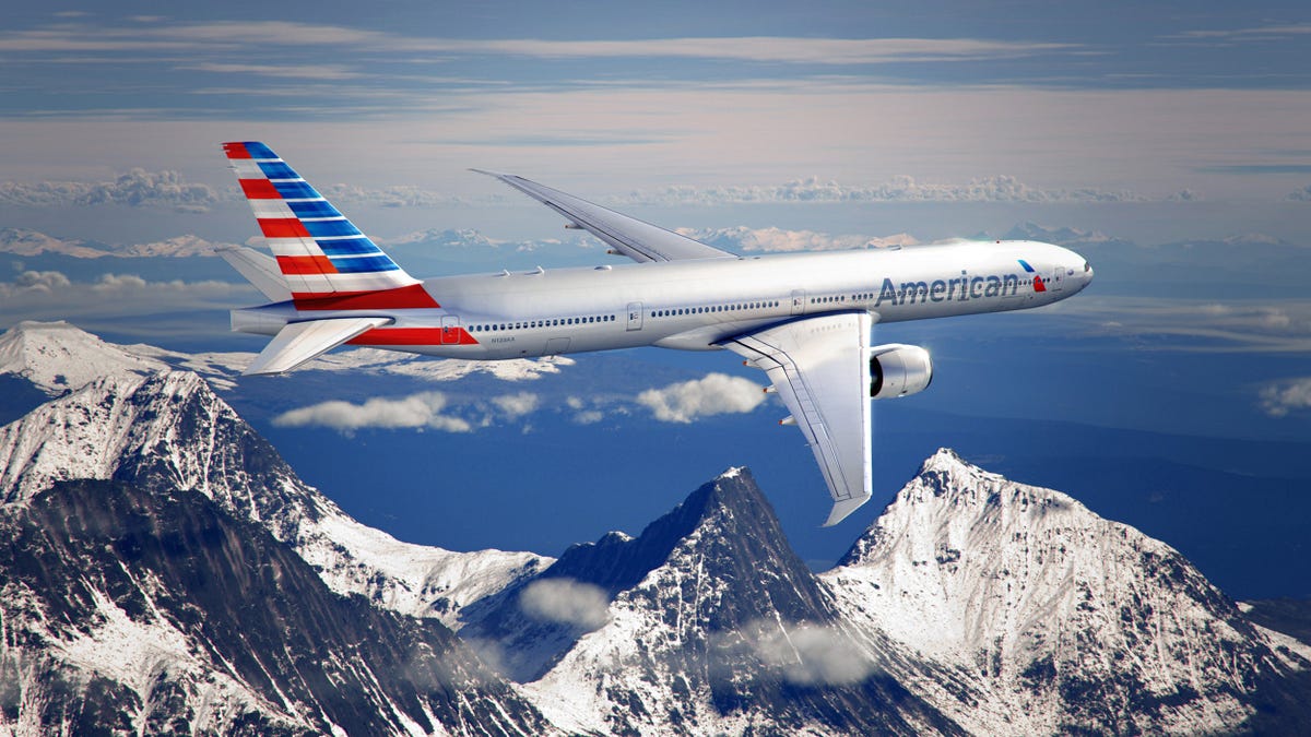 An American Airlines plane in flight, with snow-capped mountains in the background.