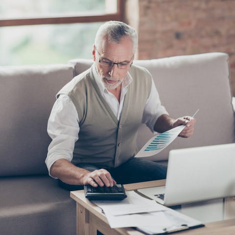 Older man sitting on couch holding document in...