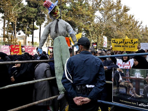 Iranian protesters dangle an Uncle Sam effigy across a barrier.