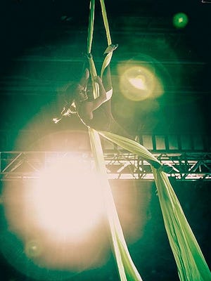 The glare of back lights nearly obscuring her and hanging by sashes secured above, a performer executed acrobatic maneuvers.
