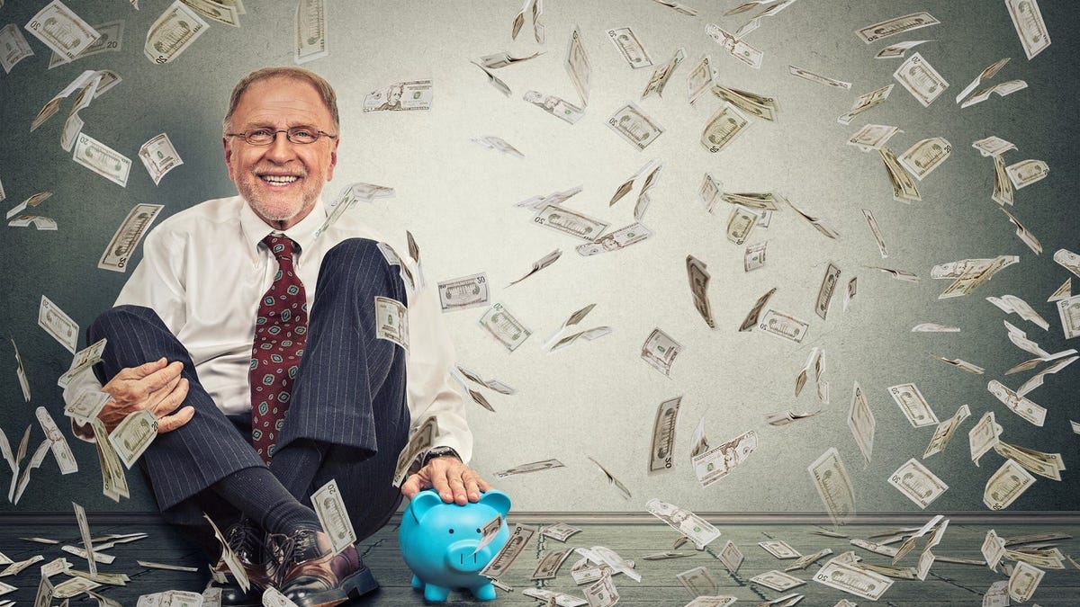 Sitting man with his hand on a piggy bank, smiling as cash falls from above.