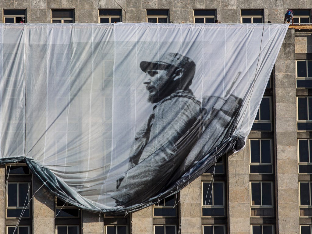 Men hang a giant banner of Cuba's late leader Fidel Castro as a young revolutionary, from the Cuban National Library building in Havana. Cuba's government declared nine days of national mourning after Castro died Nov. 25, 2016.