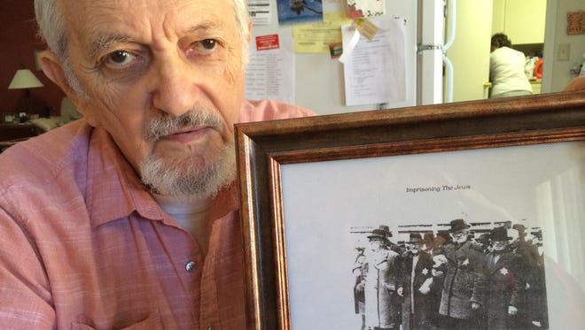 Holocaust survivor Edward Heisler, with a picture showing his father, Samuel, on the day the family arrived via cattle car at Auschwitz-Birkenau. Samuel (third from the left), along with Heisler's mother Sara, were among six million Jews murdered during the Holocaust.
