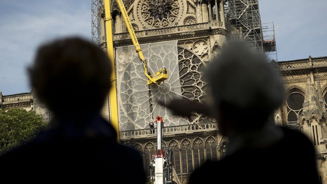 People watch Sunday as workers affix a net to cover one of the iconic stained glass windows of Notre Dame Cathedral in Paris. Some streets around the cathedral reopened, allowing the public to get a closer look after last week’s blaze.