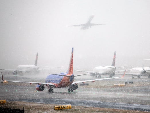 Planes line up on the tarmac as snow falls, delaying