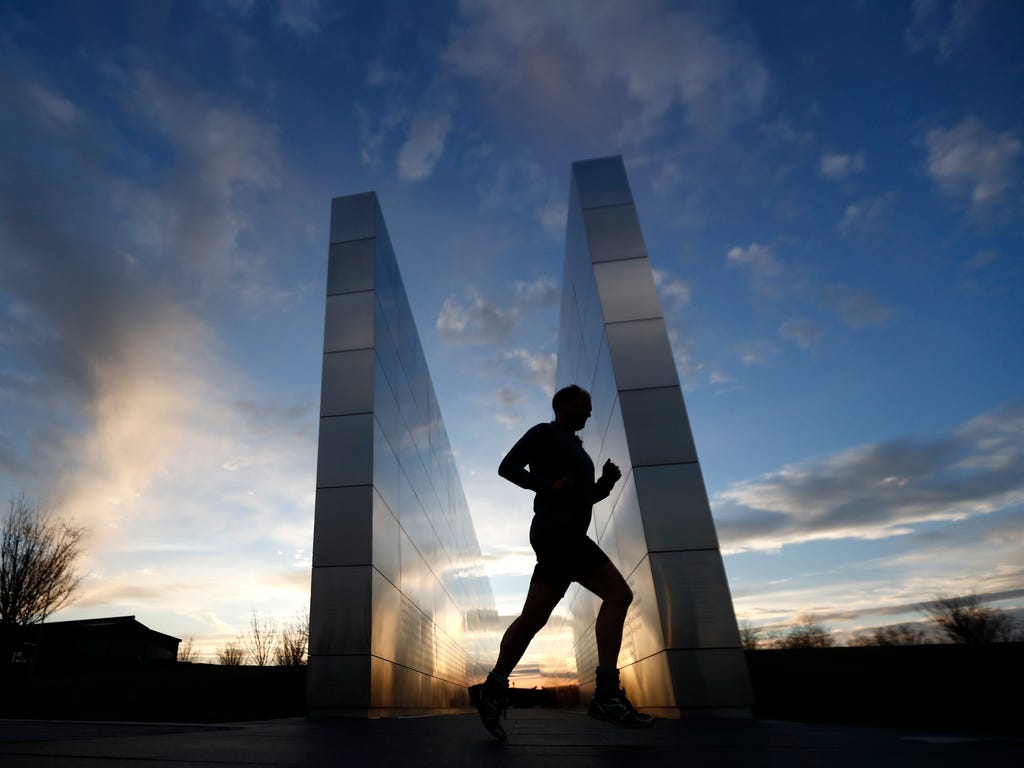 The sun sets behind a jogger trotting by the Empty Sky Memorial at Liberty State Park,  in Jersey City, N.J. The northern New Jersey region, which experienced temperature in the 60s, is bracing for a snowstorm expected to arrive overnight.