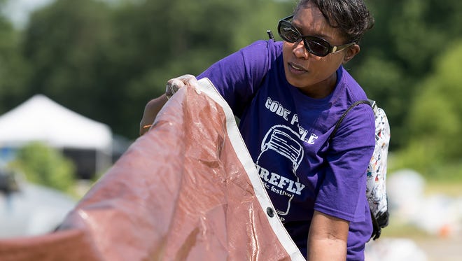 Tawana Riley, of Camden, on Monday gathers a tarp left behind by Firefly attendees that will be used to benefit Delaware's homeless population. Volunteers picked up items at the Dover music festival site that can be given to those in need.