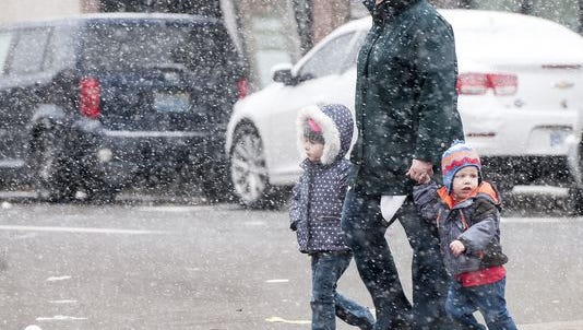A family crosses a downtown Lansing street as heavy, wet snow falls on the area Saturday.