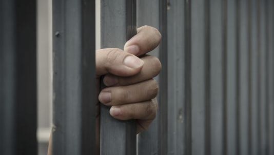 A file photo of a prisoner's hand grabbing the bars of a jail cell.