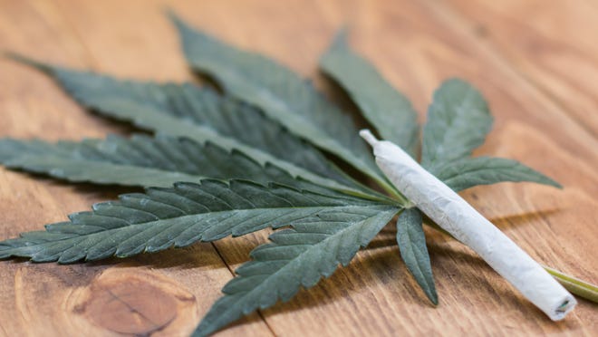 A rolled cannabis joint propped up next to a cannabis leaf on a table.
