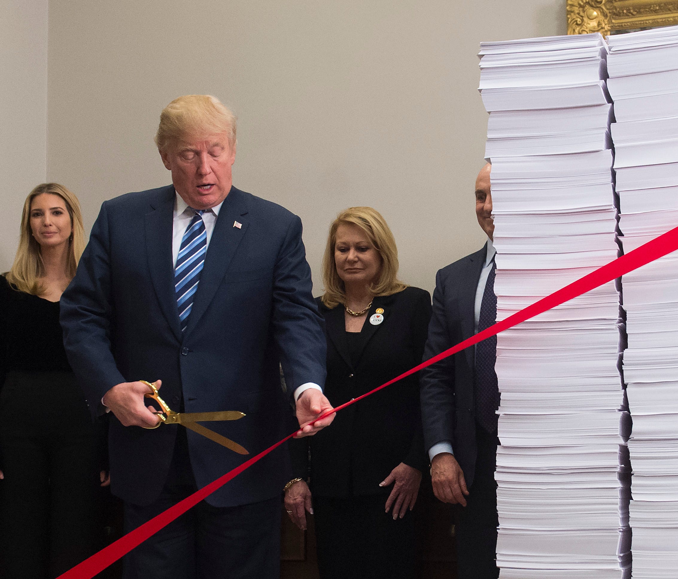 President Trump holds gold scissors Thursday as he cuts a red tape tied between two stacks of papers representing the government regulations of the 1960s and the regulations of today.