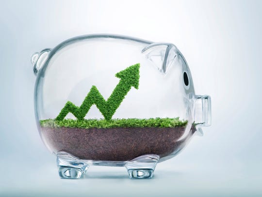 An upward-pointing arrow made of grass sticking up out of dirt inside a glass piggy bank.