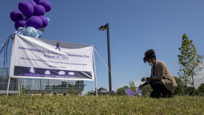 Naj Reese, an investigative secretary in the Franklin County coroner's office, marks International Overdose Awareness Day this week by planting a small, handwritten flag as a tribute to a neighbor beside a memorial to overdose victims outside the office.