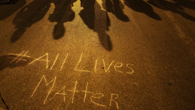 A message reading "All Lives Matter" is written on the pavement as police in riot gear cast shadows in Baltimore.