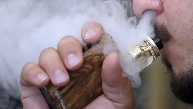 A man breathes vape from an e-cigarette at a vape shop in London in 2018.