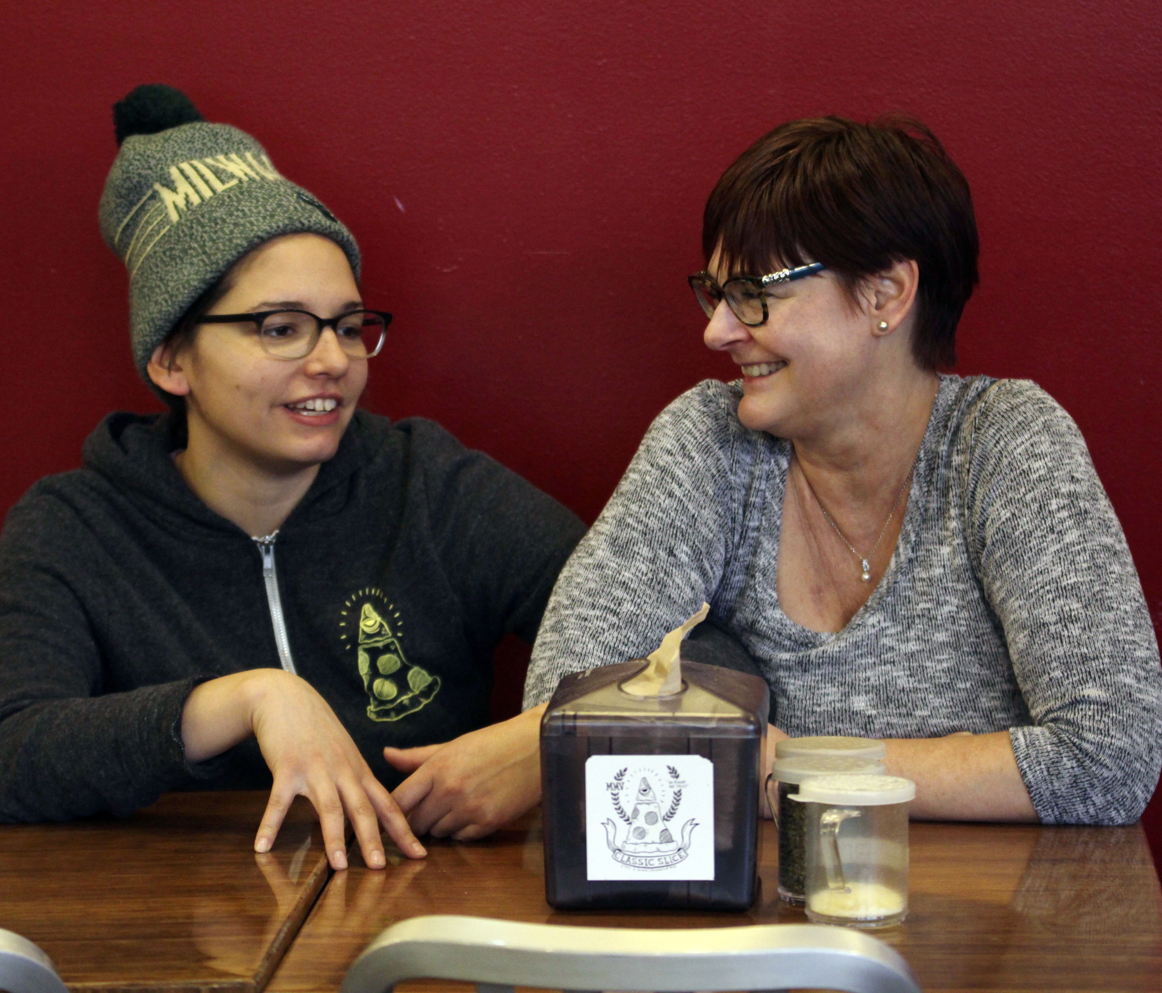 Andrea Ledesma, left, talks with her mom, Cheryl Romanowski, at Classic Slice pizza restaurant, where Ledesma works, in Milwaukee. Ledesma, 28, says her parents owned a house and were raising kids by her age. Not so for her.