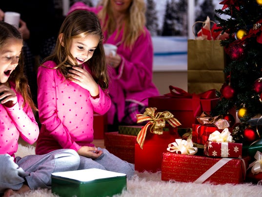 Girls excitedly open Christmas presents. Parents, tree, gifts background.