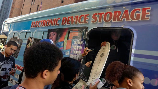 Students from Norman Thomas High School  pay a dollar to check their electronic devices, and a skateboard at a van, before school Oct. 9. New York City is preparing to end its longtime ban on cellphones in public schools, fulfilling a campaign promise of Mayor Bill de Blasio.