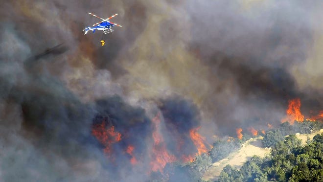 
A helicopter flies to drop water on flames just feet away from a home as crews work to protect homes in New Harmony in this 2012 file photo.
