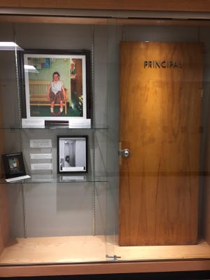 This Dec. 20, 2017, photo provided by Cambridge Central Schools shows a display case with photos, an illustration and the door that was once on the principal's office at Cambridge Central Schools in Cambridge, N.Y. Inside the case is the original door from the principal's office that served as the setting for the Normal Rockwell Saturday Evening Post cover in 1953, known as "Girl With Black Eye," or "The Shiner." Steve Butz, a science teacher at Cambridge High School, preserved the door for display after it was replaced during a renovation project.