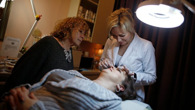 Renu Day spa owner Anna Pamula, left, watches aesthetician Isabel Kaczerzewska shape the eyebrows of client Gail Lewis on Jan. 13, 2017 in Deerfield, Ill.