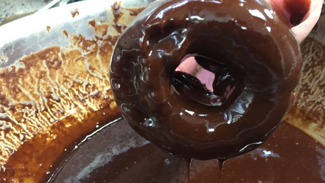 A baker dips a yeast doughnut in chocolate ganache at Rocket 88.