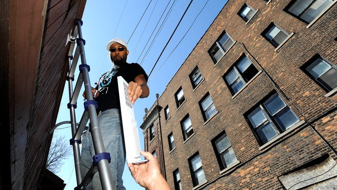 Ali Dirul, of Detroit, Ryter Cooperative Industries engineering director, prepares to install the solar-powered LED light on the garage to light up the alleyway.