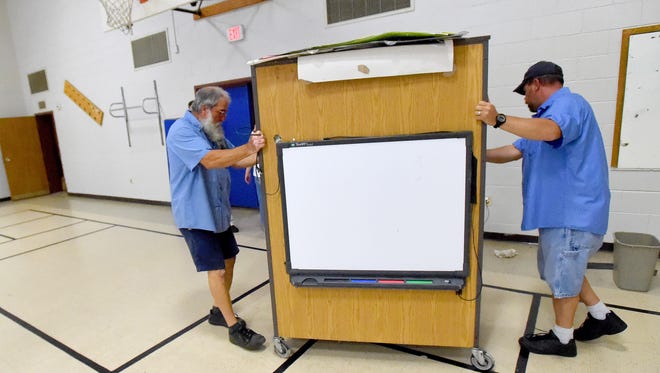 Head custodian Walter Lupachino and custodian Todd Barker wheel a rolling cabinet with a Smartboard hanging on its back from the gymnasium at Riverheads Elementary School on Wednesday, July 22, 2015. They need to repair one of the cabinet's wheels. The board's location on the cabinet's back was a compromise on how to get one within the gym for use by the physical education teacher. "It's simple but good," said Lupachino. "Have to work with what we have."