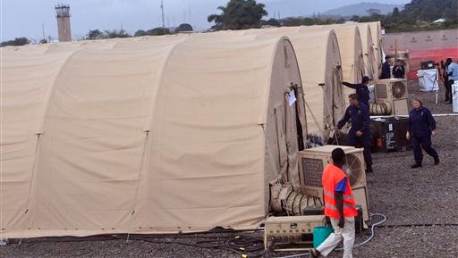 In this photo taken Wednesday  Nov. 5, 2014, on the outskirts of the city of Monrovia, Liberia, health workers walk around medical tents that form part of a new American clinic to be used for the treatment of people suffering from the Ebola virus. As the Ebola epidemic flares in new hot spots and dims in others, the response to its shifts must catch up, experts say, and that’s a challenge because it is a slow process for governments to authorize aid, to gather it together and then deliver it. And to build treatment units, even rudimentary ones, takes even more time. By the time it’s built, the outbreak may have moved elsewhere. (AP Photo/Abbas Dulleh)