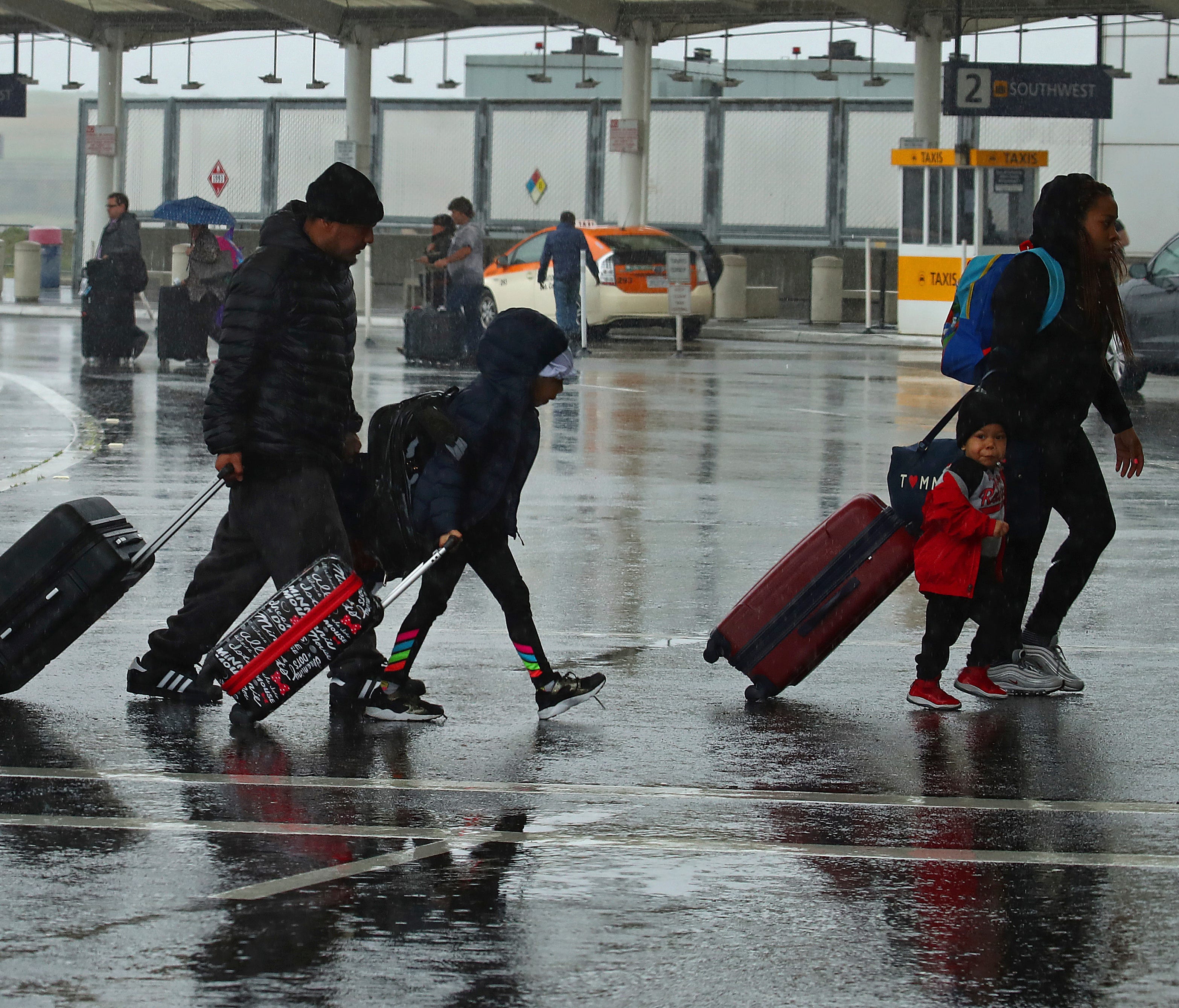 Travelers walk during a rainstorm to the terminals at Oakland International Airport on April 6, 2018, in Oakland, Calif.