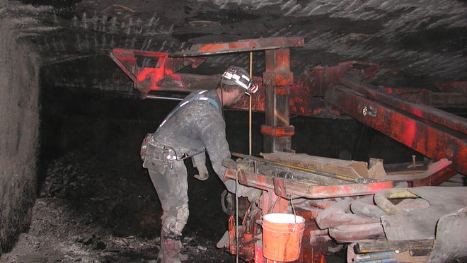 A coal miner puts bolts up to support a mine roof.