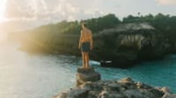 Man standing on a cliff in front of the ocean wear