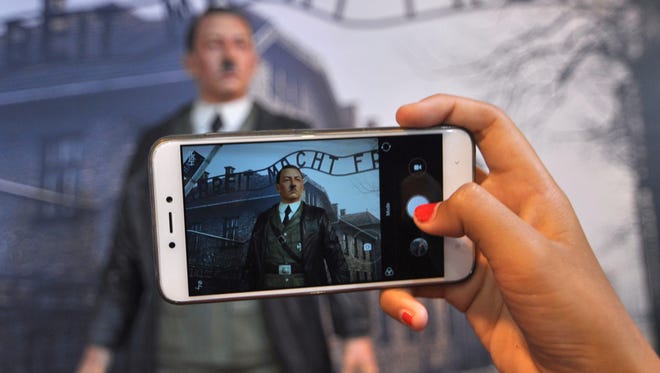 In this Wednesday, Nov. 8, 2017 photo, a visitor uses her mobile phone to take a photo of the wax figure of Adolf Hitler displayed against the backdrop of an image of Nazi Death Camp Auschwitz-Birkenau at De Mata Museum in Yogyakarta, Indonesia. Rights groups have expressed outrage over the display calling it "sickening" and demanded its immediate removal.