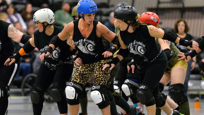 The Pin-Up Prowlers' Dede Gaetz, who goes by the roller derby name of Mia Capricious (blue helmet, center) and teammates Piper Poundher (left) and Head Trauma Helen set up a block during a bout with the Gargoyle Brigade on Saturday at the River's Edge Convention Center.