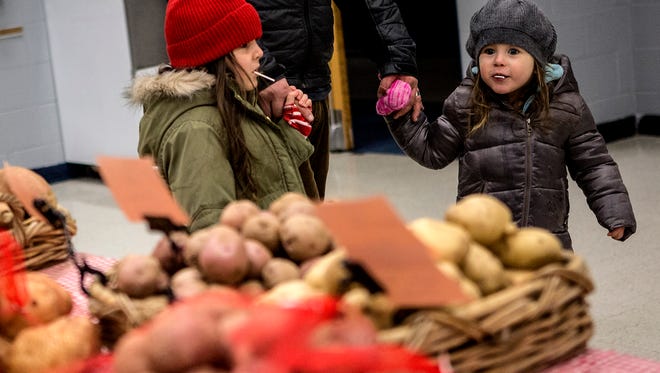 Adeline and Eliza Baldwin walk past a table of potatoes and other winter vegetables for sale at the Granville Winter Market. 