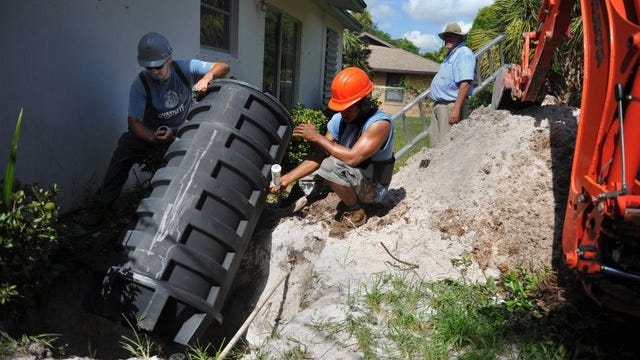 Stuart Public Works Department workers (from left) Johnathon Molina and Joel Zelaya install a grinder tank sewage system along with team leader Corky Kossen (background) in the backyard of a home on North Riverpoint Road in Stuart on Aug. 22, 2014. The grinder tank is a low pressure sewer pump system that replaces a septic system.